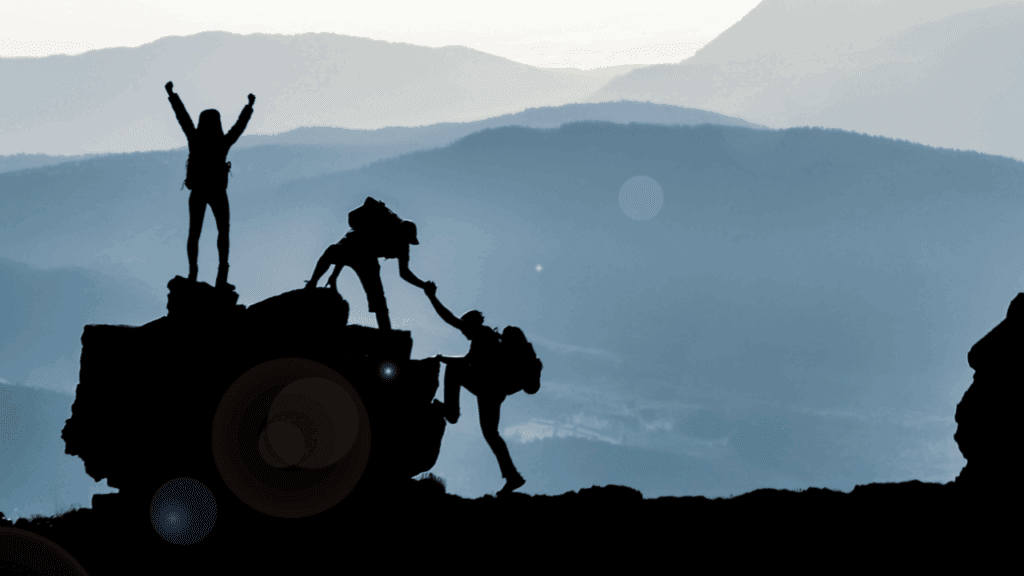 Three people on a mountain top, celebrating career success after motherhood with hands joined in unity and support.