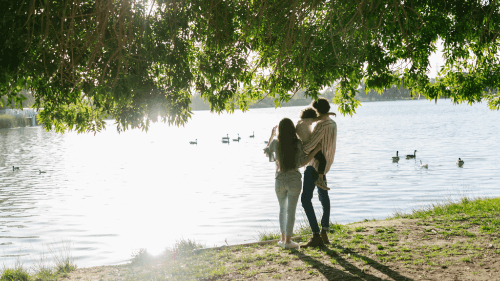 Two people stand under a tree by a lake, sharing a peaceful moment during their healing process.
