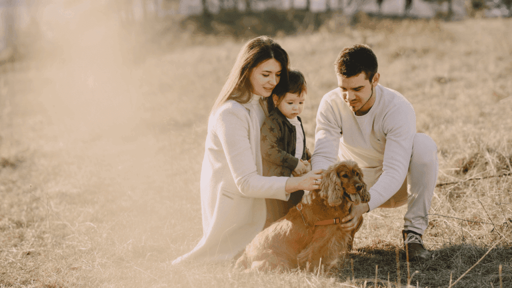 A happy family with their dog enjoying a sunny day in a lush green field, surrounded by nature.