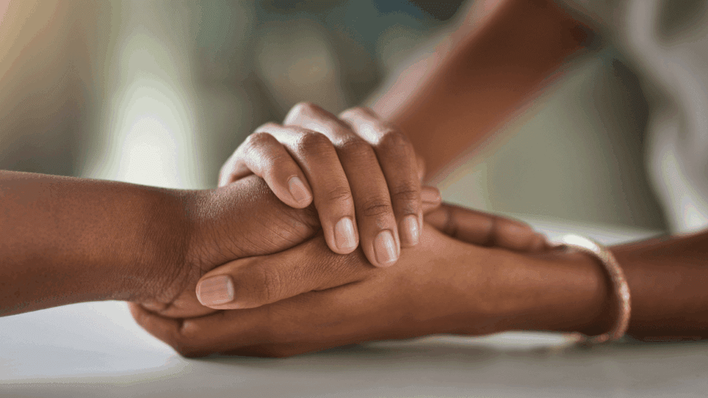 Two hands gently clasped together over a table, symbolizing connection and support in the context of self-abandonment.